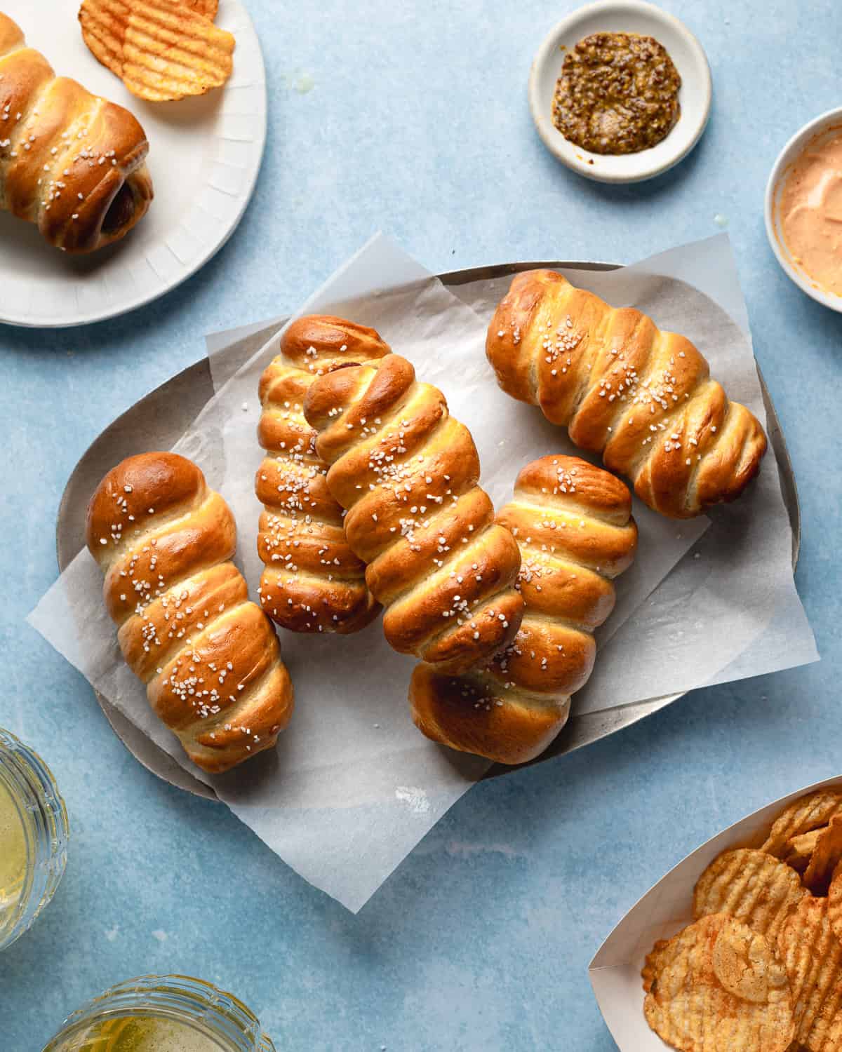 Pretzel dogs stacked on a metal platter lined with parchment paper with mustard in a small sauce plate. 