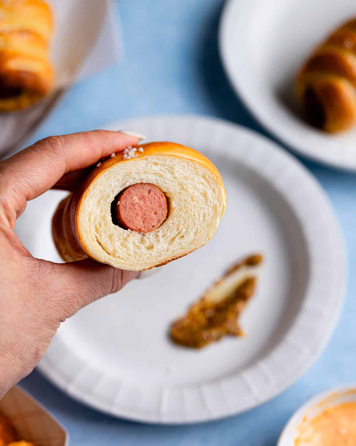 Hand holding a pretzel dog sliced in half revealing crumb and hot dog. 