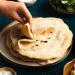 Hand folding a tortilla on stack of tortillas.