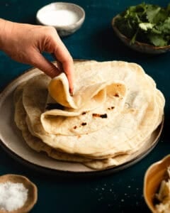 Hand folding a tortilla on stack of tortillas.