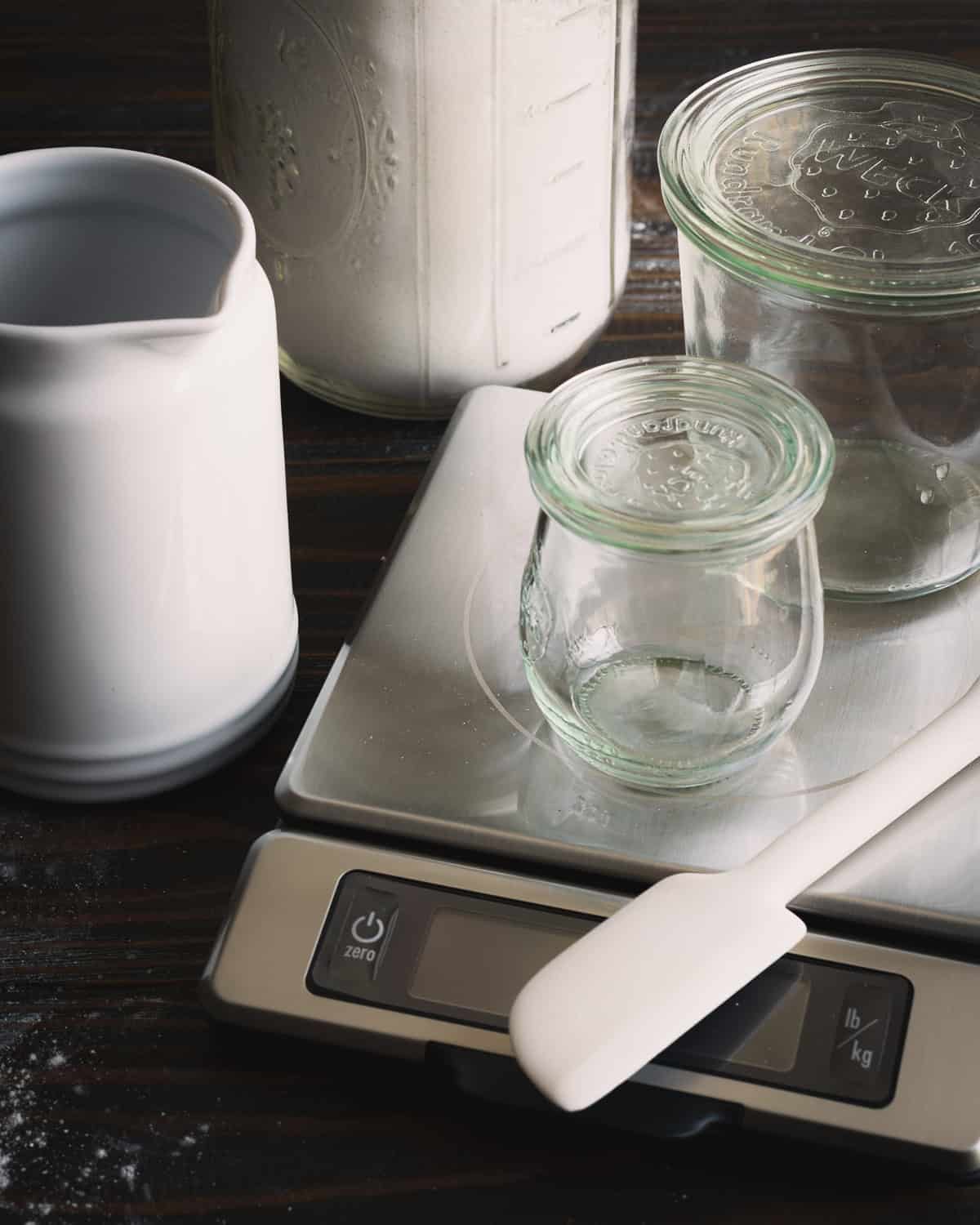 Tools for sourdough starter. Pitcher, jars, spatula, scale and all-purpose flour.