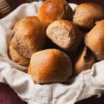 Dinner rolls in a basket lined with a tea towel.