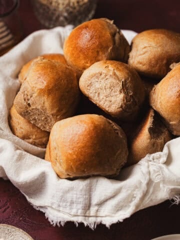 Dinner rolls in a basket lined with a tea towel.