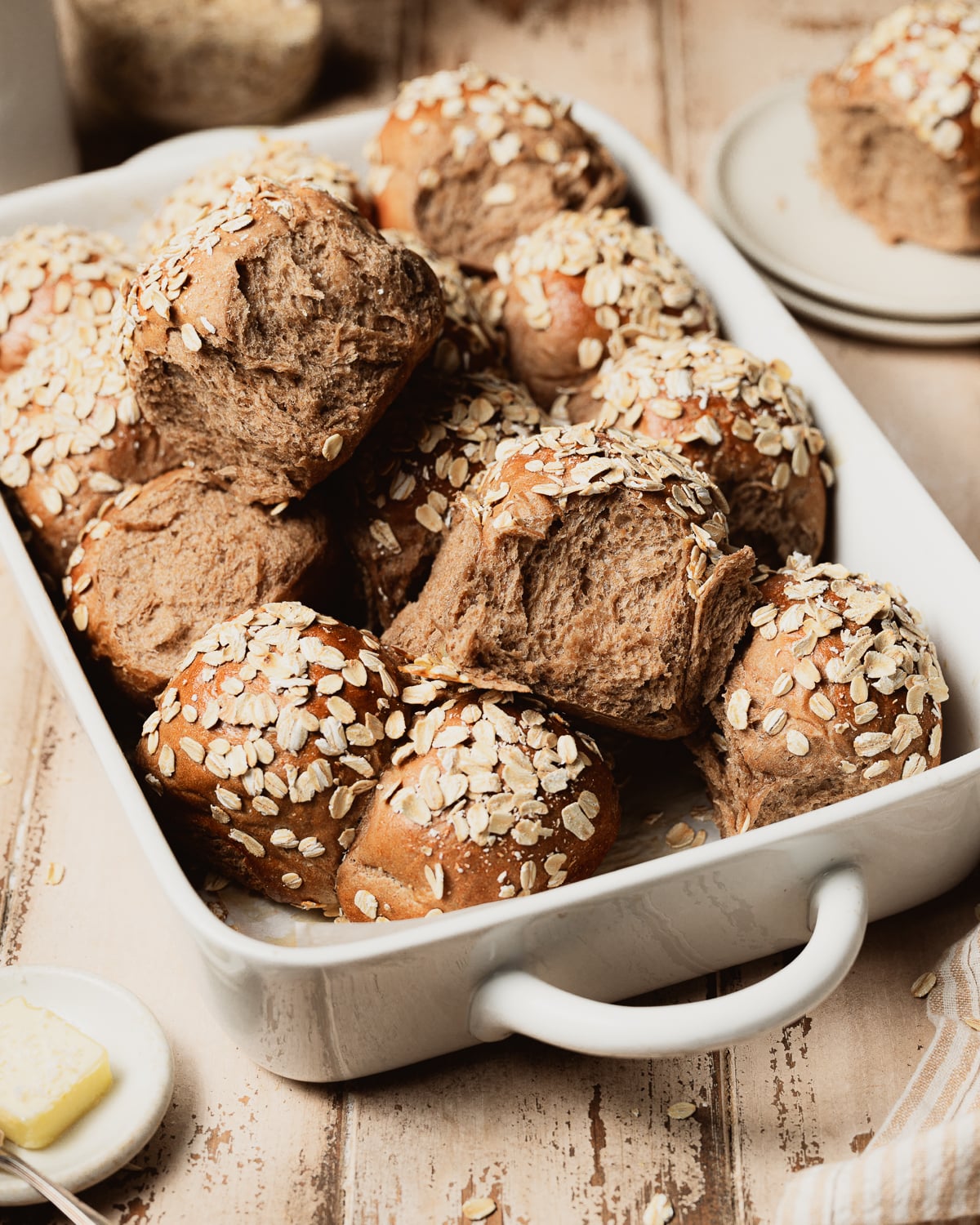 Brown rolls topped with oats in a ceramic baking dish.