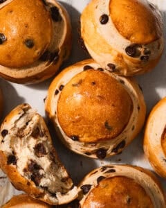 Chocolate chip brioche buns on a piece of parchment paper with one torn in half.