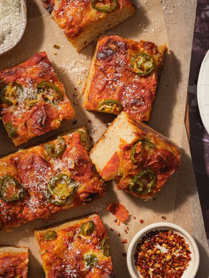 Sliced focaccia pizza on a parchment-lined cutting board.