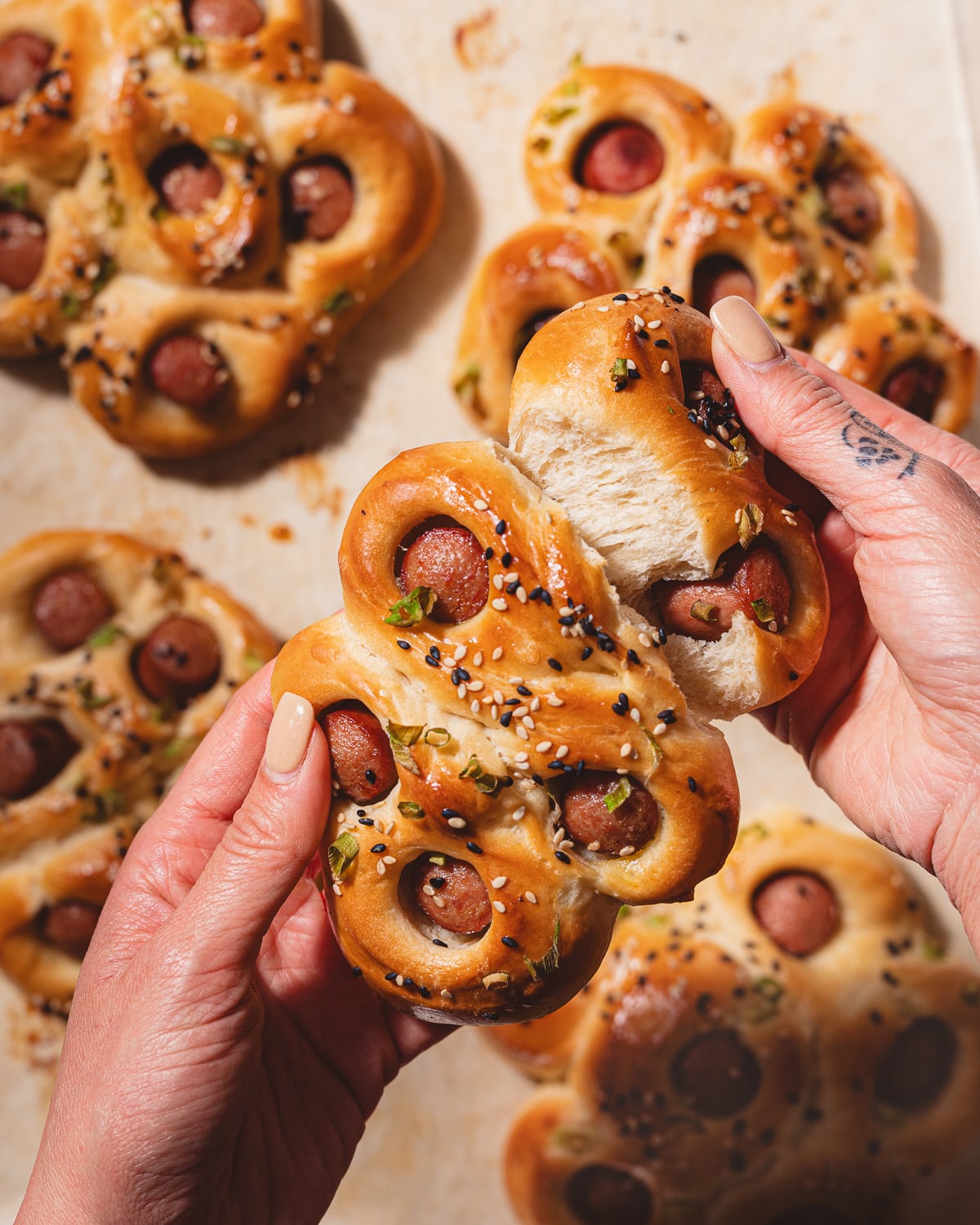 Hands tearing pieces off of a hot dog flower bun. 