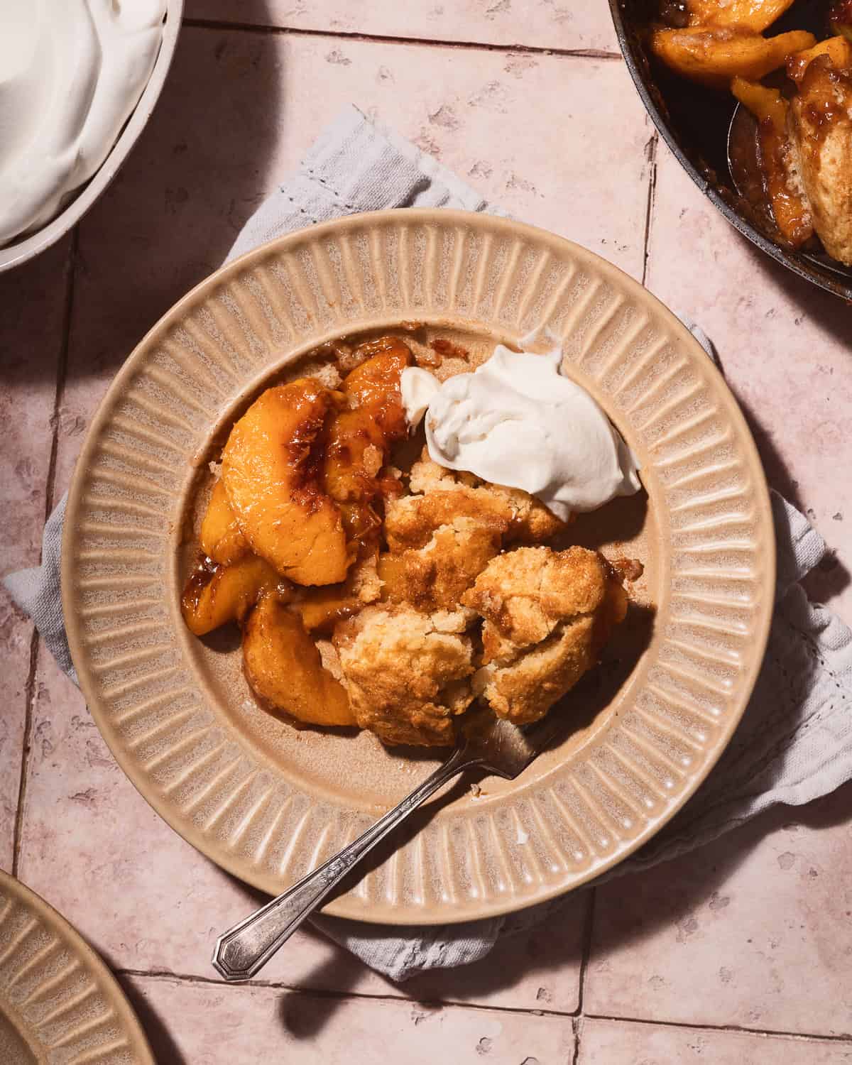 Piece of peach cobbler on a small plate with whipped cream.