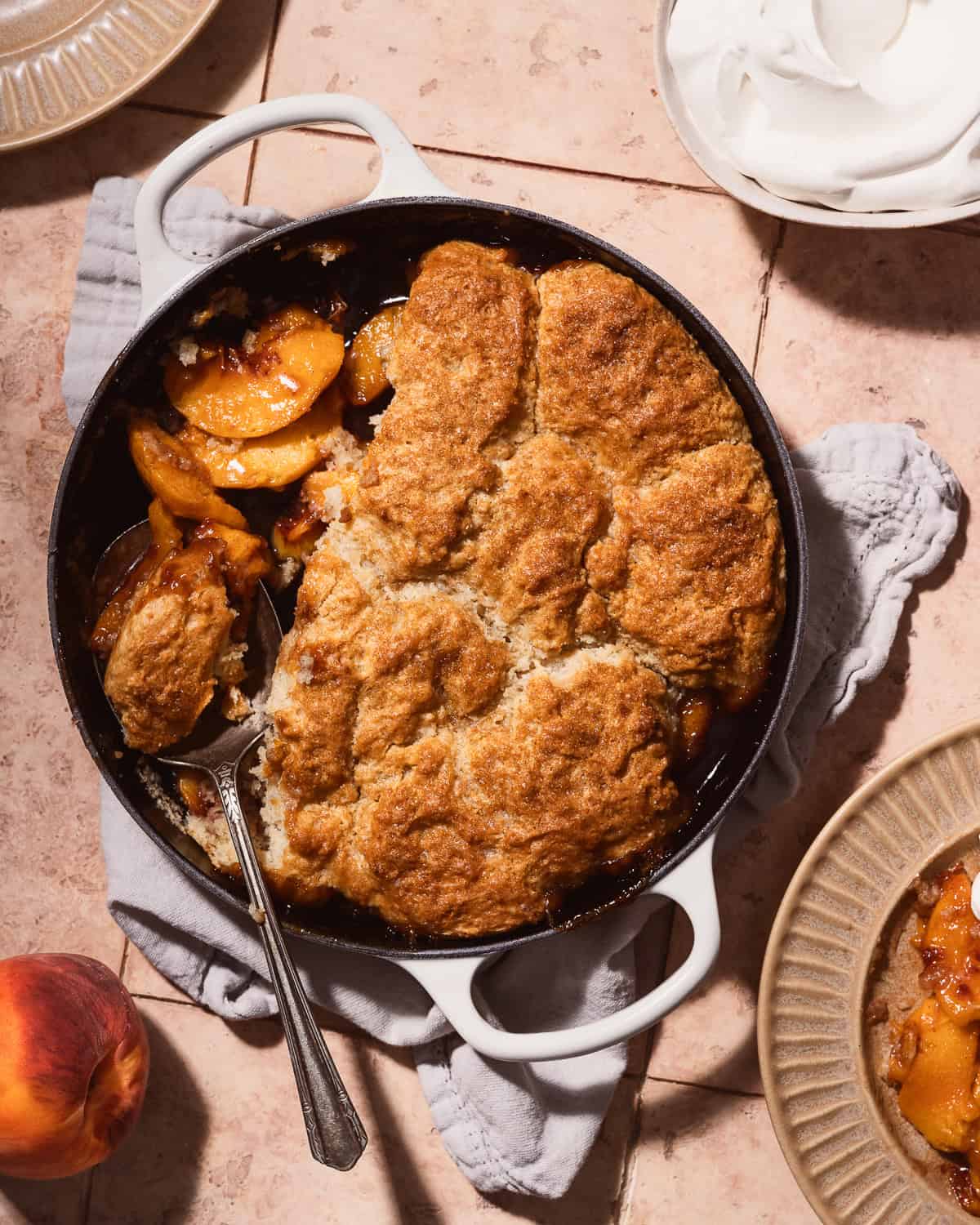 Spoon scooping out a piece of peach cobbler from a skillet.